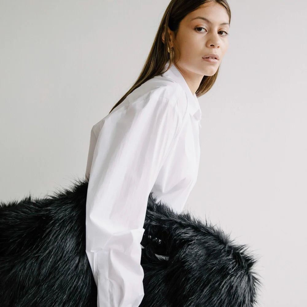 Woman wearing a white shirt with a black fur Bag on a plain background